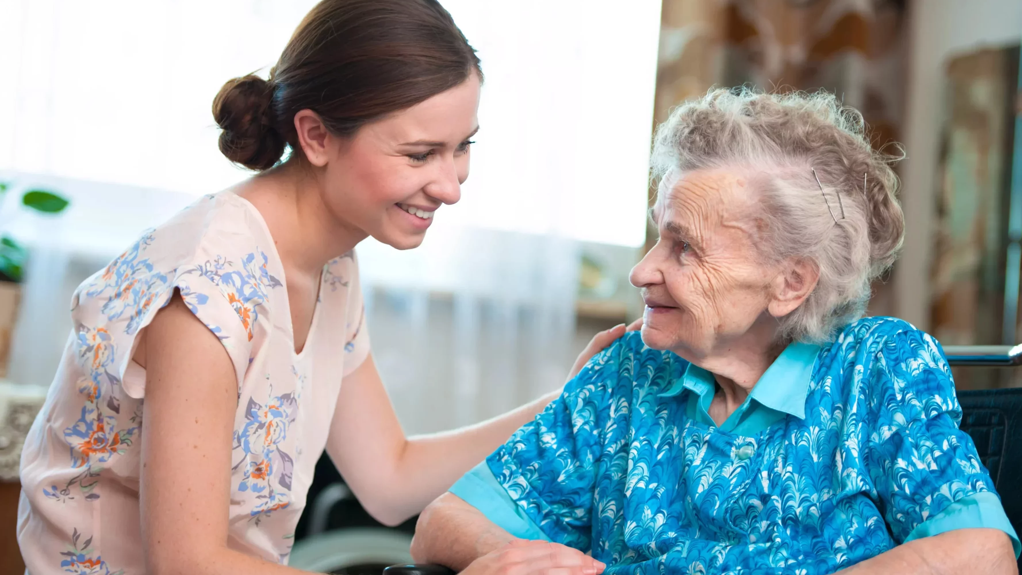 Symbolfoto von 5min.at: Pflegerin kümmert sich rührend um eine Seniorin im Rollstuhl.