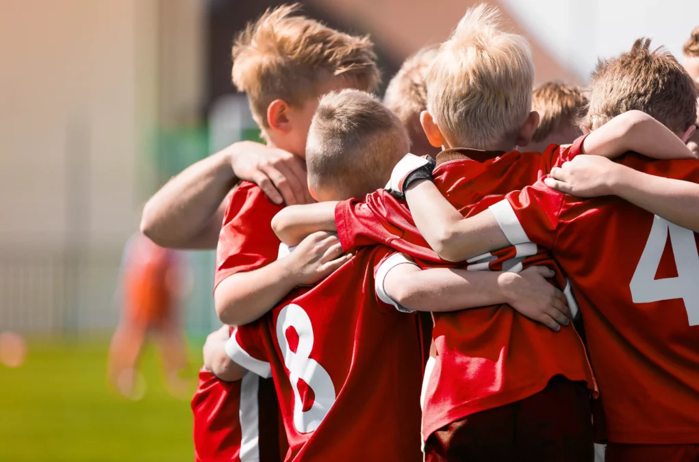 Symbolfoto von 5min.at: Kinder stehen im Fußballtrikot am Platz zusammen.