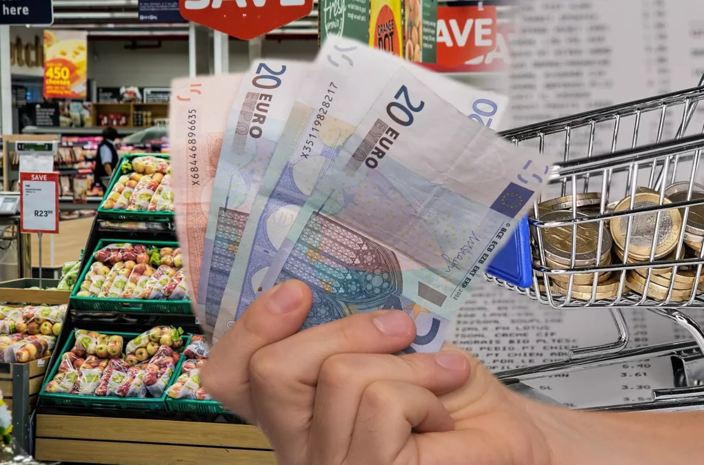 Symbolfoto zu einem Beitrag von 5min.at: Eine Hand hält Geldscheine, im Hintergrund ein Gemüseregal im Supermarkt, und eine Grafik eines Einkaufwagens voller Münzen
