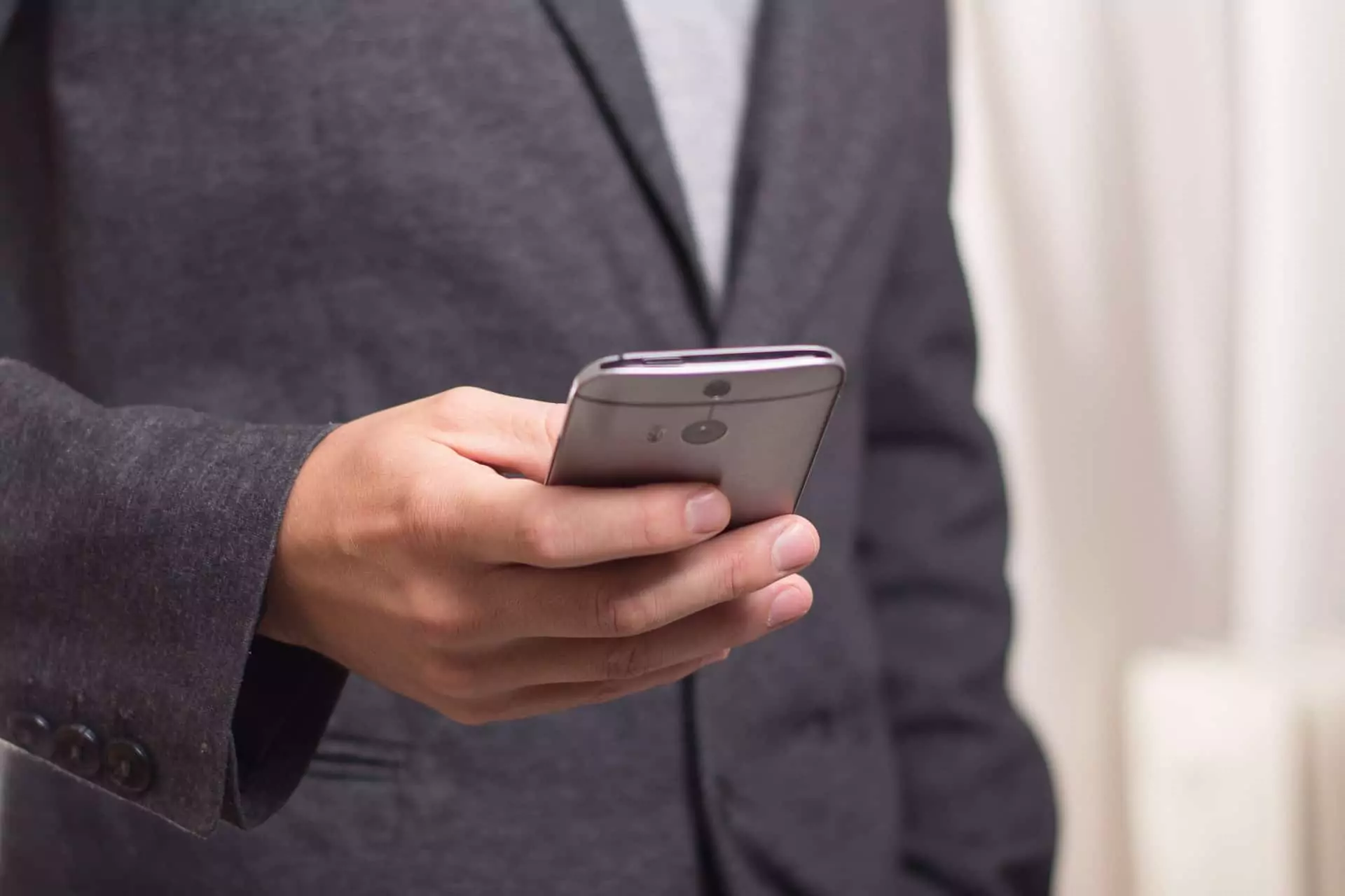 Symbolfoto zu einem Beitrag von 5min.at: Ein Mann im Anzug hält ein Handy in der Hand