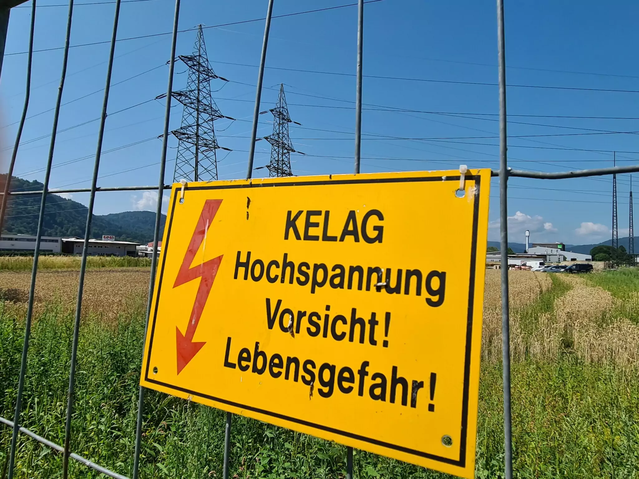 Symbolfoto zu einem Beitrag von 5min.at: Hochspannung! Vorsicht Lebensgefahr! Ein Schild der KELAG vor Hochspannungsleitungen