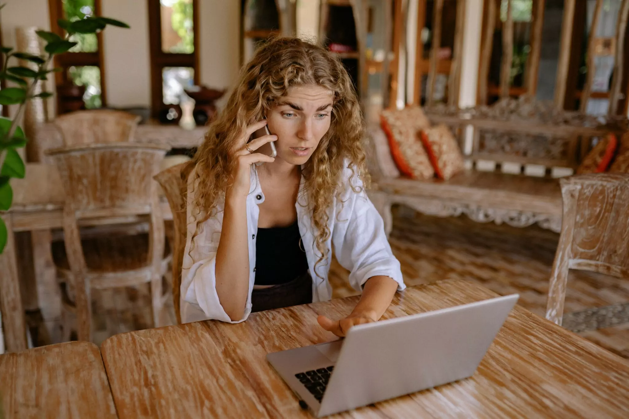 Symbolfoto zu einem Beitrag von 5min.at: Eine Frau sitzt an einem Tisch, auf dem ein Laptop steht, und telefoniert