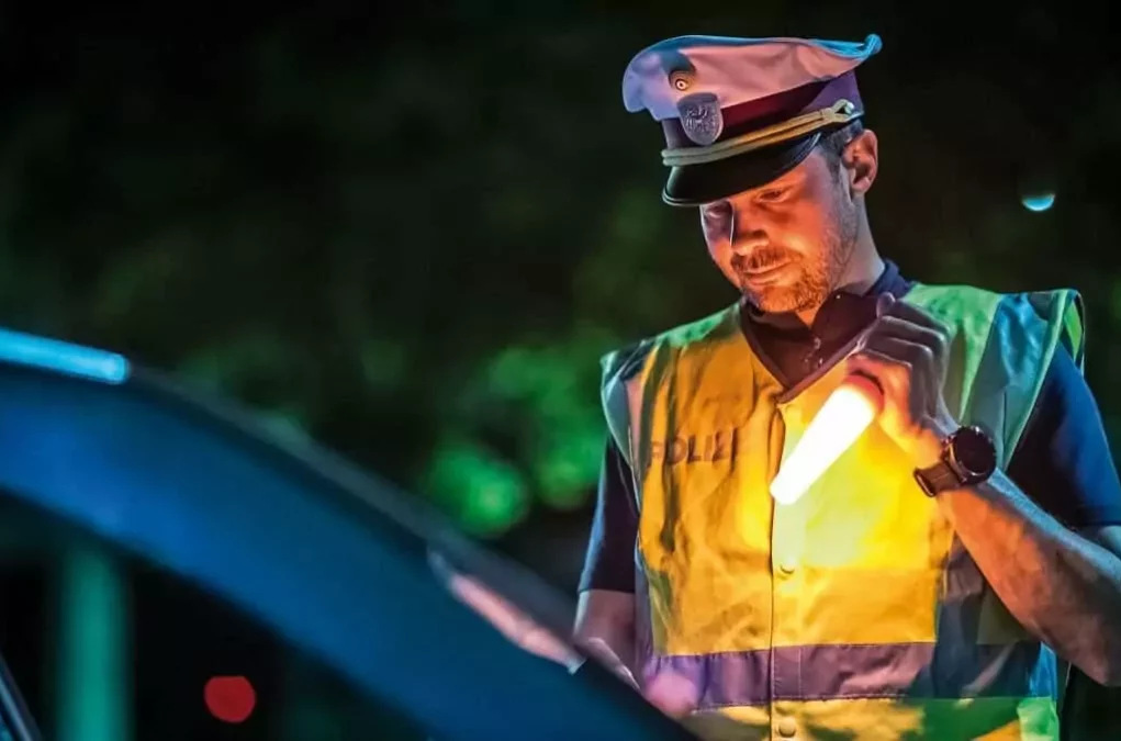 Symbolfoto zu einem Beitrag von 5min.at: Ein Polizist kontrolliert ein Auto bei Nacht