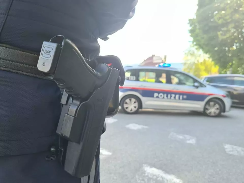 Symbolfoto zu einem Beitrag von 5min.at: Ein Villacher Polizist von hinten, man sieht seine Waffe