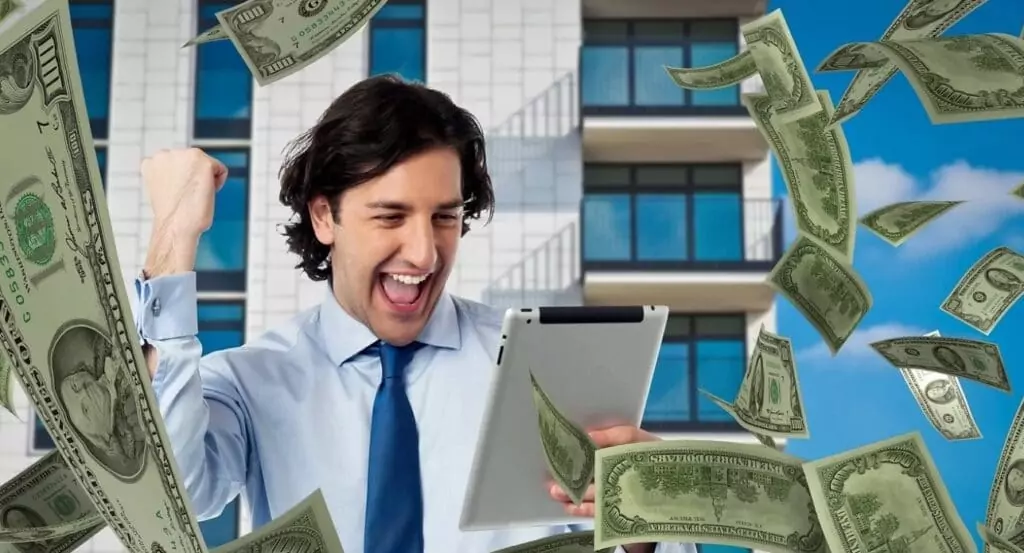 Symbolfoto von 5min.at: Mann sieht auf ein Tablet und freut sich über einen Geldgewinn.