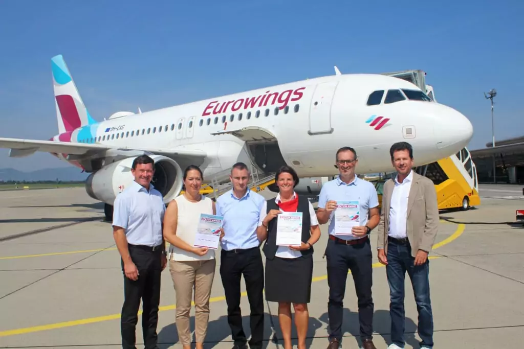 Symbolfoto von 5min.at: Sechs Personen stehen vor einen Eurowings Flugzeug am Flughafen Graz.