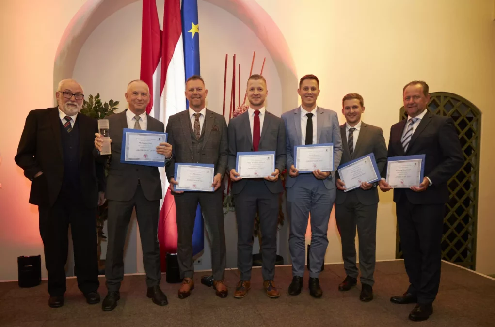 Zu sehen sind 6 Männer in Anzug mit Preisen in den Händen