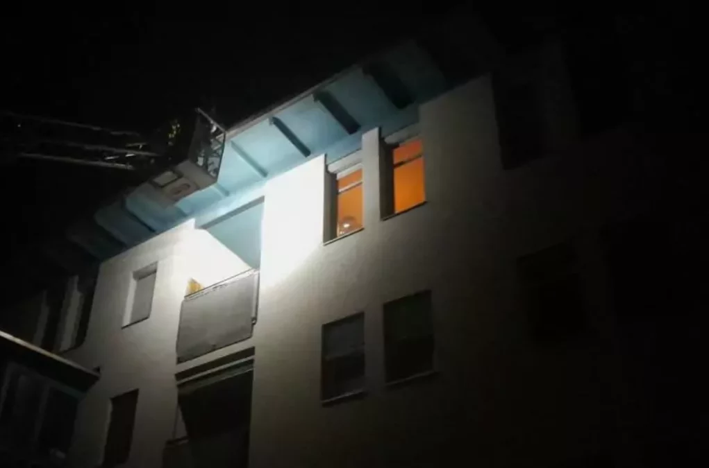 Bild bei Beitrag von 5min.at: Zu sehen ist ein Gebäude bei Nacht und im Dunkeln die Feuerwehrleiter, die die betroffene Wohnung inspiziert.