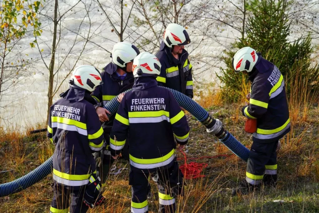 Ein Bild auf 5min.at zeigt mehrere Florianis in Einsatzuniform. Sie versuchen eine Wasserleitung, von einem nahen Fluss zur angeblichen Einsatzstelle zu legen.
