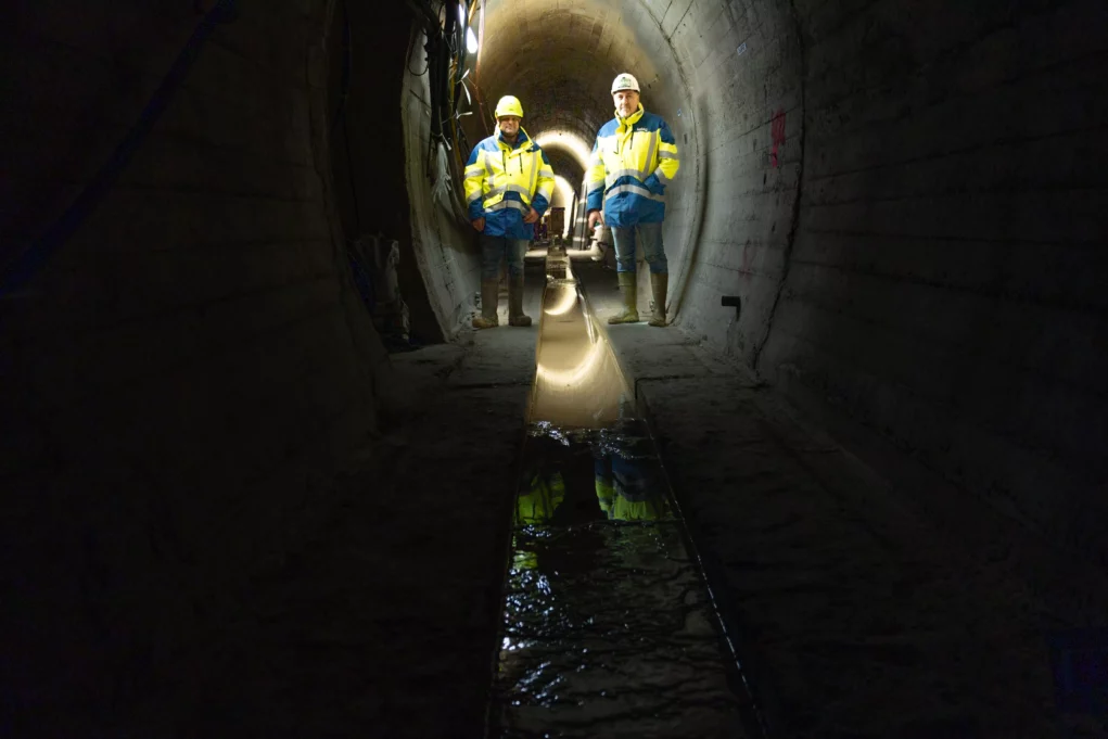 Foto auf 5min.at zeigt Arbeiter in einem Tunnelsystem unter einem Wasserdamm.