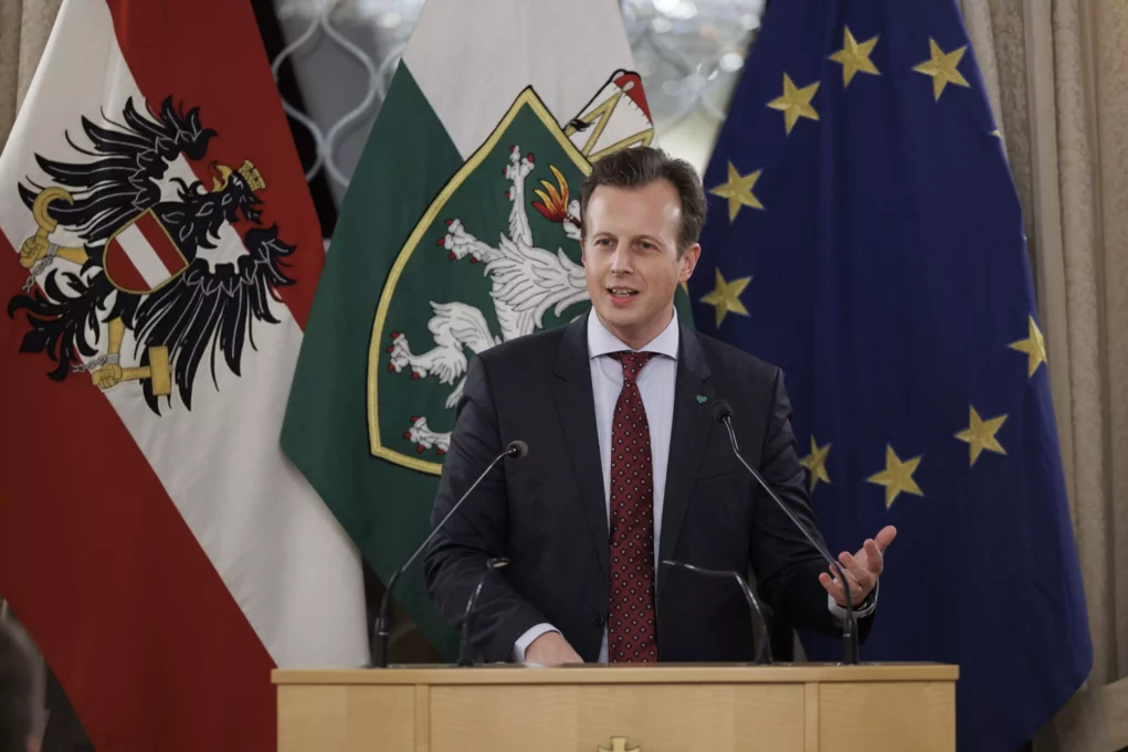 Das Bild auf 5min.at zeigt: Ein Mann steht am Rednerpult und hält eine Rede; im Hintergrund die Flaggen der Republik