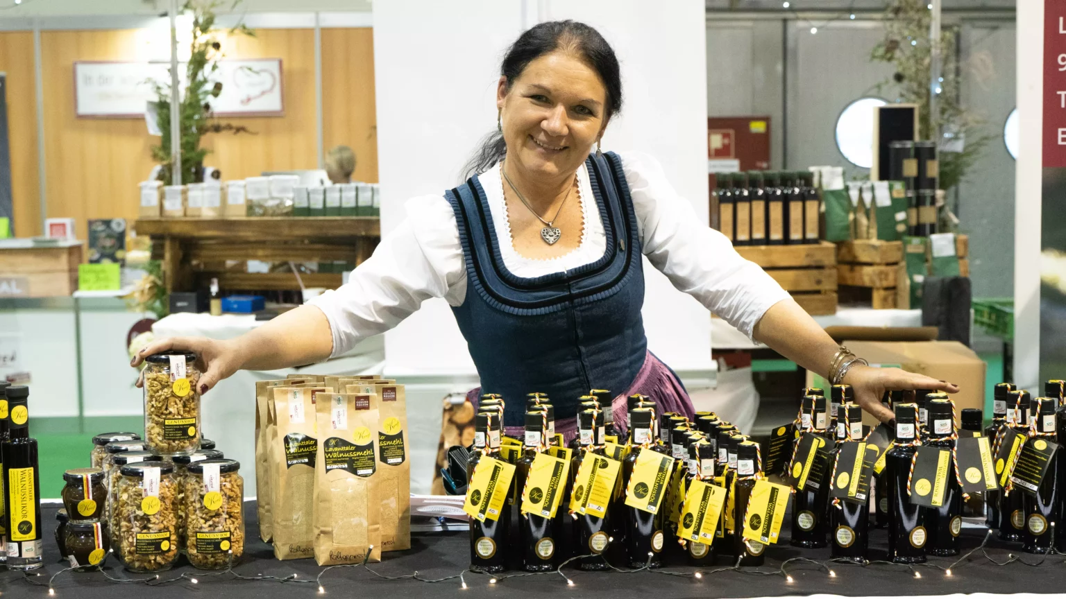 Foto in Beitrag von 5min.at: Zu sehen ist eine Frau vor vielen regionalen Sachen. Sie hat ein Dirndl an.