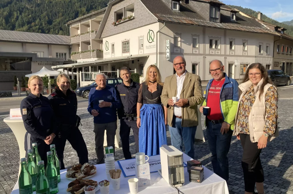 Foto in Beitrag von 5min.at: Mehrere Menschen vor dem Bahnhofsgebäude sind zu sehen. Sie stehen vor einem Tisch.