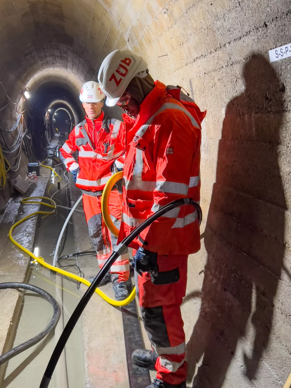 Foto auf 5min.at zeigt Arbeiter in einem Tunnelsystem unter einem Wasserdamm.