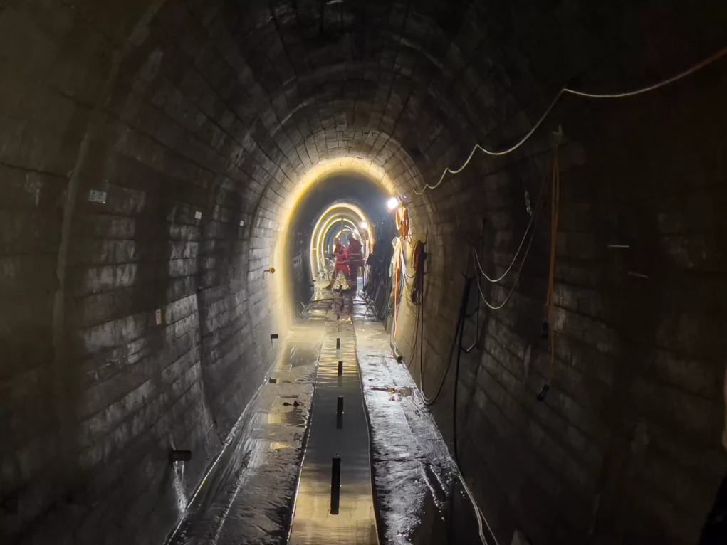 Foto auf 5min.at zeigt Arbeiter in einem Tunnelsystem unter einem Wasserdamm.