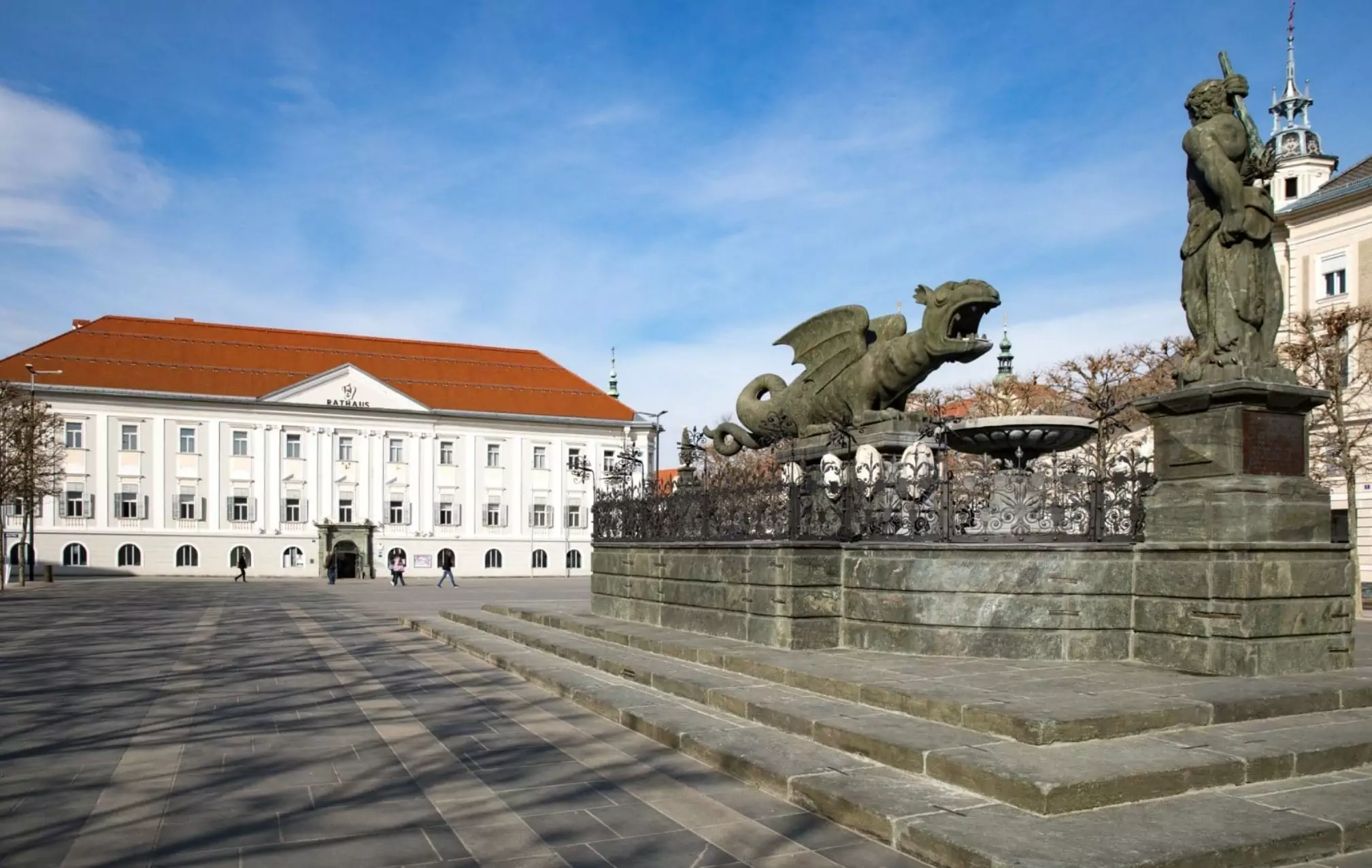 Ein Bild auf 5min.at zeigt den Klagenfurter Lindwurm am Neuen Platz. Dahinter steht das Rathaus.