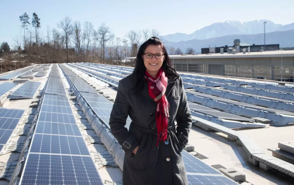 Ein Bild auf 5min.at zeigt Landesrätin Sara Schaar in einem dicken schwarzen Mantel. Sie steht vor einer Photovoltaik-Anlage.
