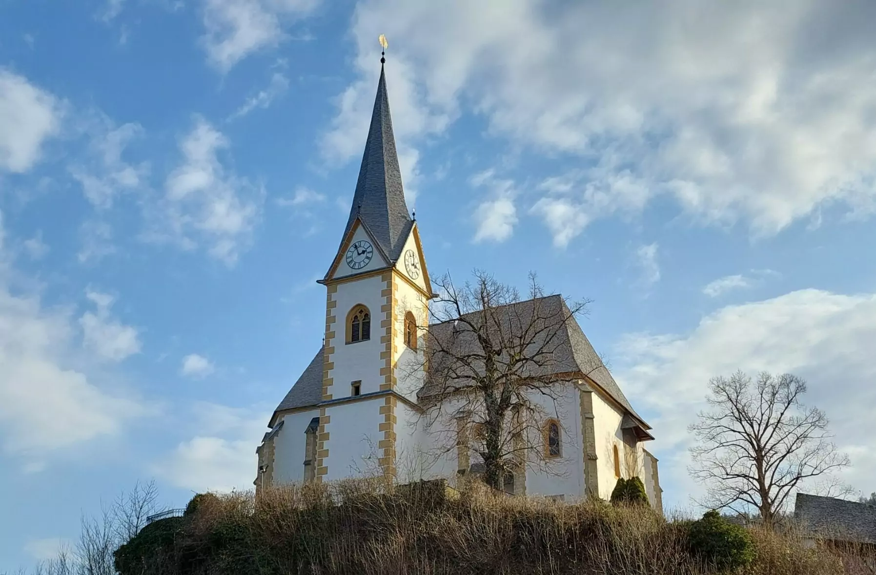 Ein Bild auf 5min.at zeigt die Kirche auf einer Anhöhe in Maria Wörth. Dahinter ist blauer Himmel, mit einigen Wolken dazwischen.
