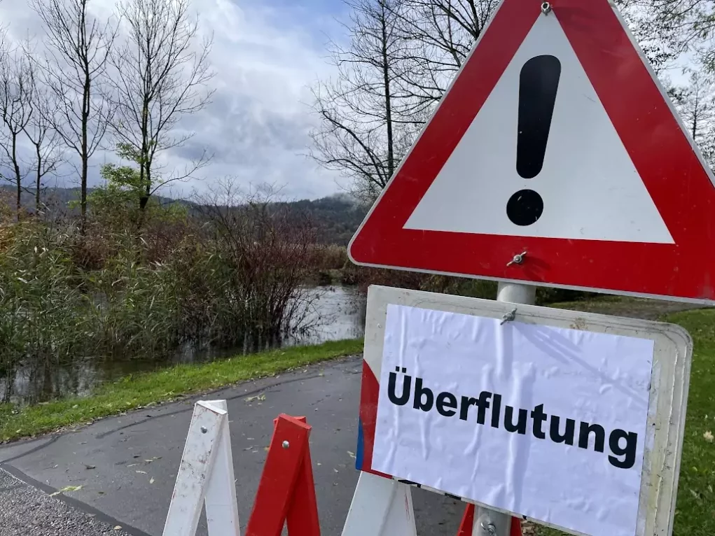 Bild auf 5min.at zeigt einen über die Ufer getretenen Fluss, samt Schild mit Aufschrift "Überflutung".
