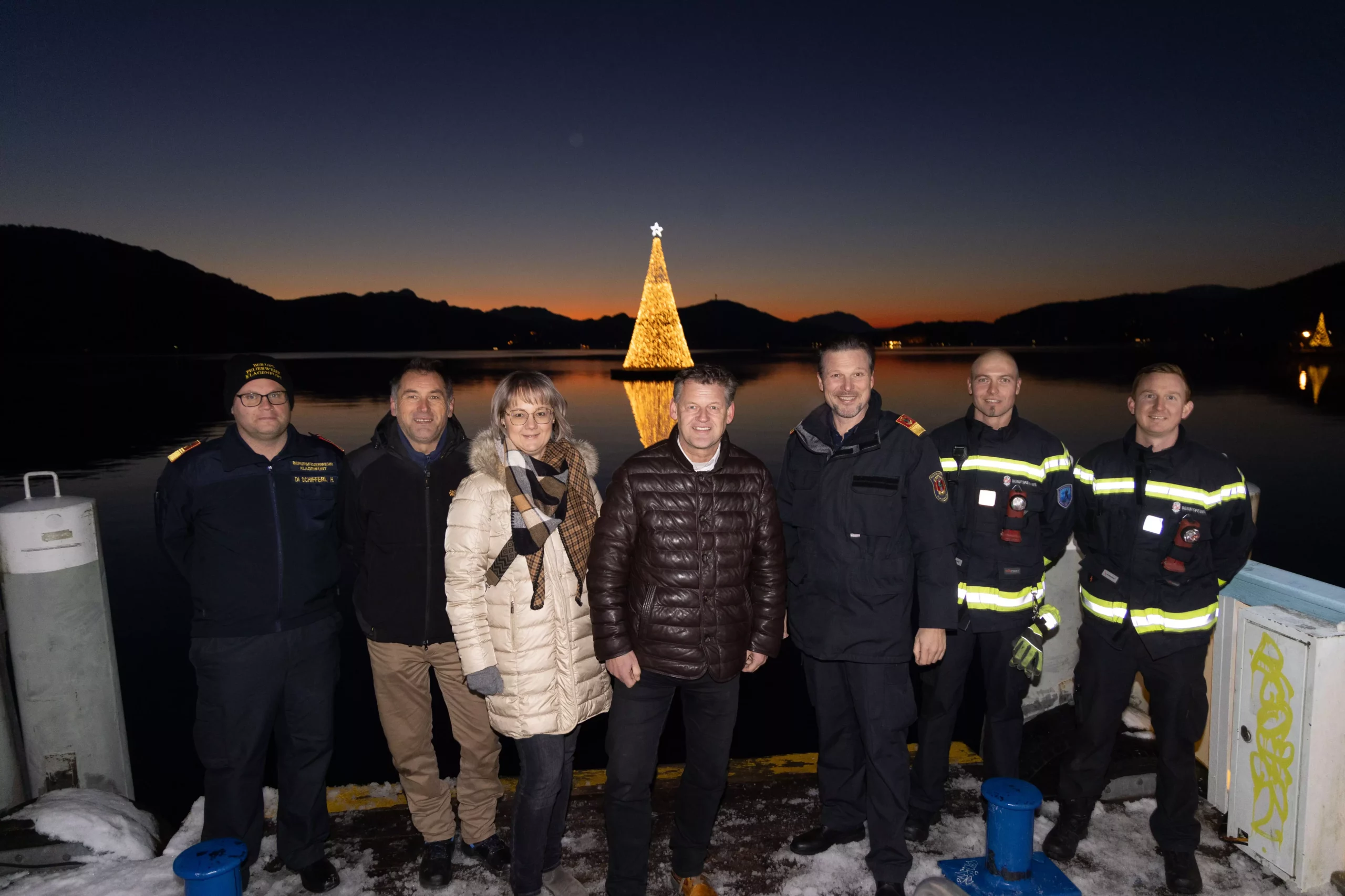 Ein Bild auf 5min.at zeigt Branddirektor Herbert Schifferl, Dragan Arsič und Elisabeth Kos vom Stadtgarten, Bürgermeister Christian Scheider, Branddirektor Stv. Wolfgang Germ und die Einsatztaucher Stephan Holzer und Philipp Pirker vor dem schwimmenden Christbaum.