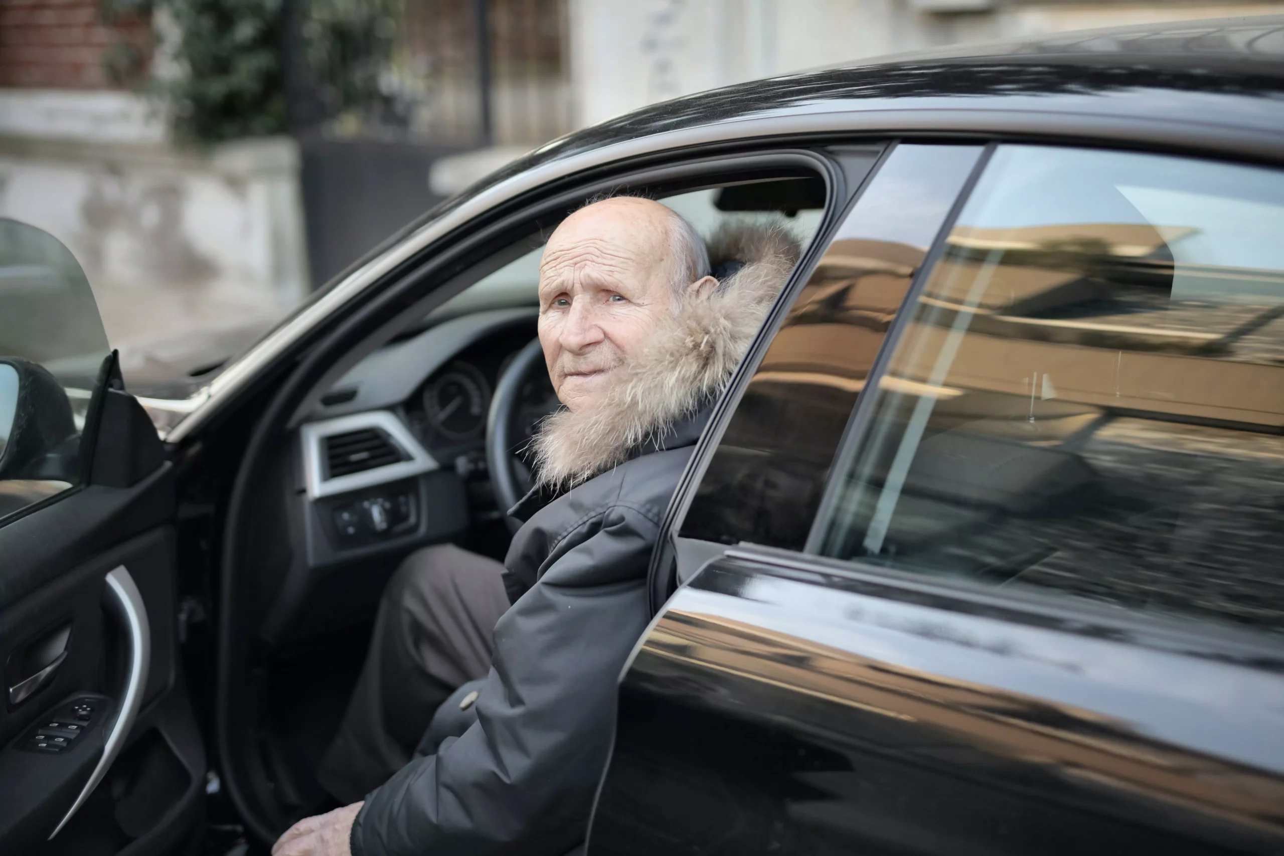 Foto in Beitrag von 5min.at: Zu sehen ist ein alter Mann, der gerade aus dem Auto aus oder einsteigt und in die Kamera schaut.