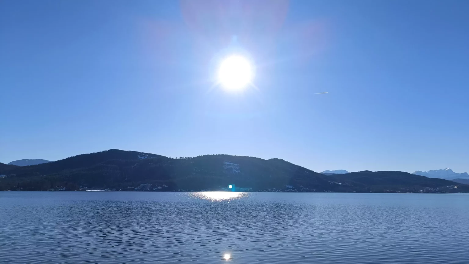 Ein Bild auf 5min.at zeigt das blaue Wasser des Wörthersees im Winter. Der Himmel ist strahlend blau, die Sonne scheint.