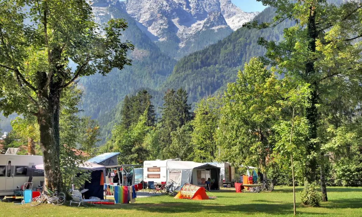 Foto in Beitrag von 5min.at: Zu sehen sind mehrere Campingzelte und -fahrzeuge vor einem malerischen Hintergrund.