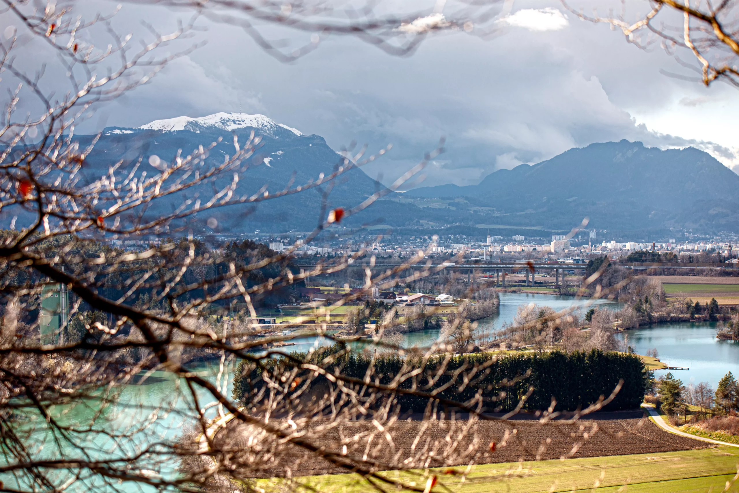 Ein Bild auf 5min.at zeigt die Drau. Dahinter erheben sich die Stadt Villach und der Dobratsch.