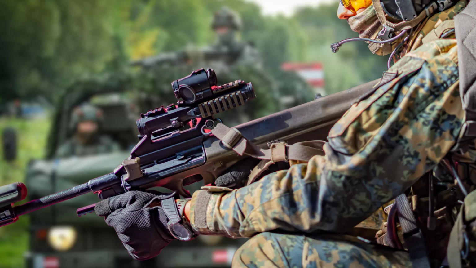 Ein Bild auf 5min.at zeigt vollbesetzte Fahrzeuge des österreichischen Bundesheers. Im Vordergrund steht ein Sturmgewehr.