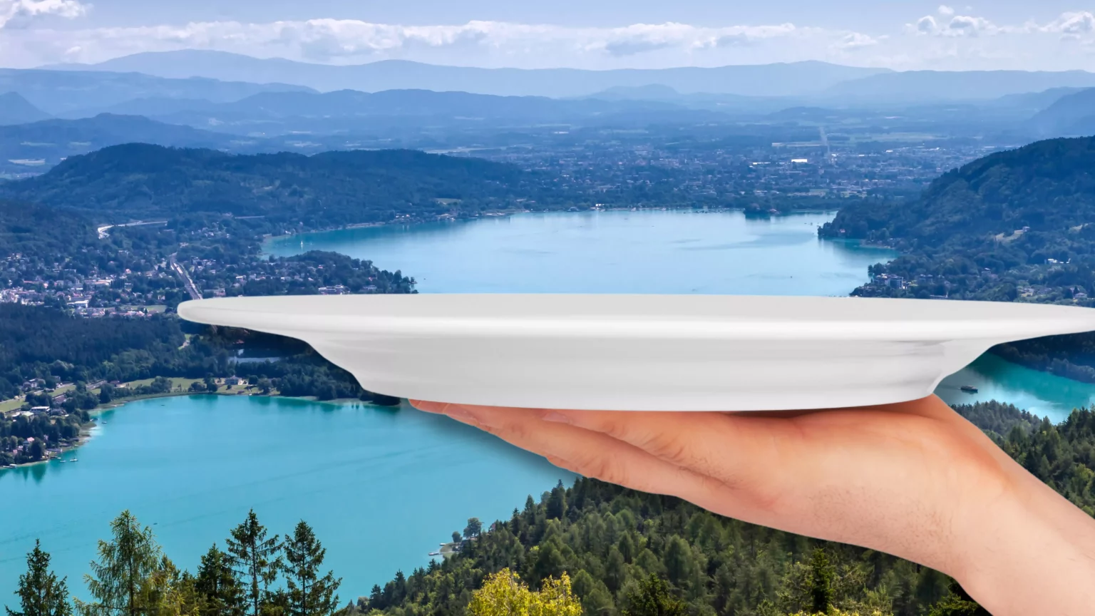 Ein Bild auf 5min.at zeigt eine Hand, die einen Teller hält, vor dem Wörthersee.