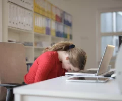 Foto in Beitrag von 5min.at: Zu sehen ist eine Frau, die an einem Tisch sitzt und verzweifelt ihren Kopf auf die Tastatur des Laptops gelegt hat.