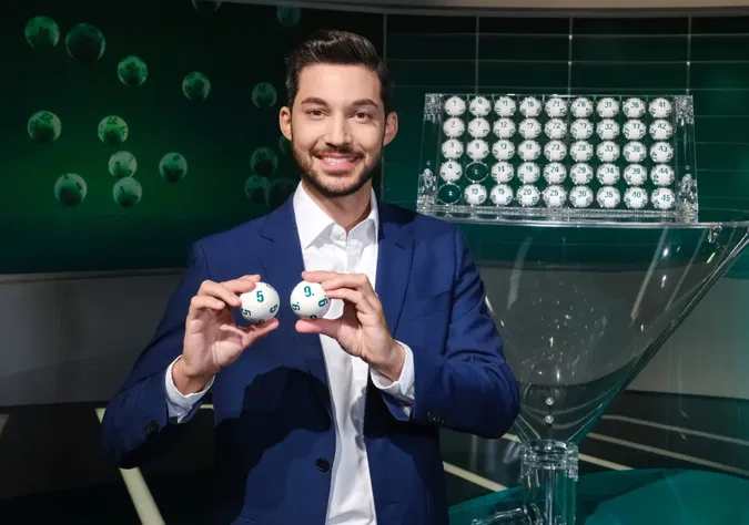 Ein Bild auf 5min.at zeigt ORF-Moderator Marcel Kilic mit zwei Lotto-Bällen.