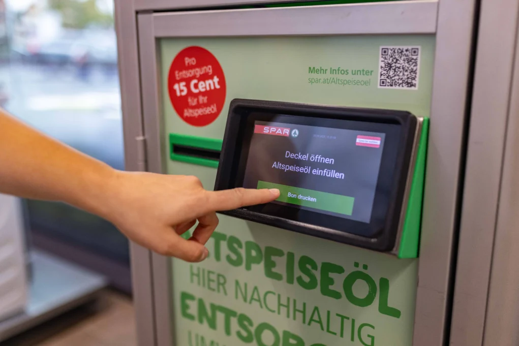 Foto in Beitrag von 5min.at zeigt einen Finger, der auf einen "Knopf" beim Sammelautomaten für Altspeiseöl drückt.