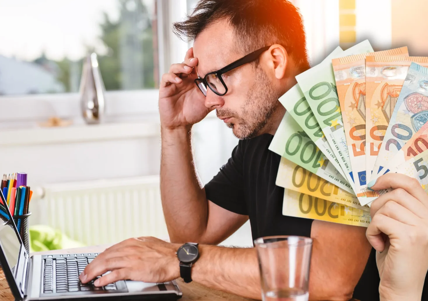 Foto in Beitrag von 5min.at zeigt im Vordergrund eine Hand mit mehreren Euroscheinen, im Hintergrund eine Person vor einem Laptop, der angestrengt auf den Bildschirm schaut.