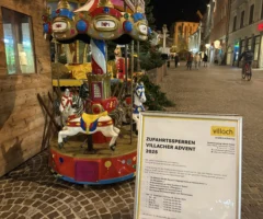 Das Bild auf 5min.at zeigt einen Flyer und im Hintergrund ein Kinderkarussell am Villacher Adventmarkt.