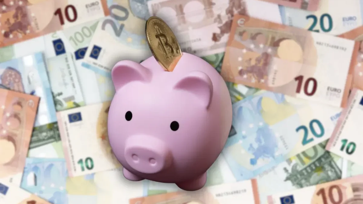Foto auf 5min.at zeigt Geld und ein Sparschwein mit einer Kryptomünze.