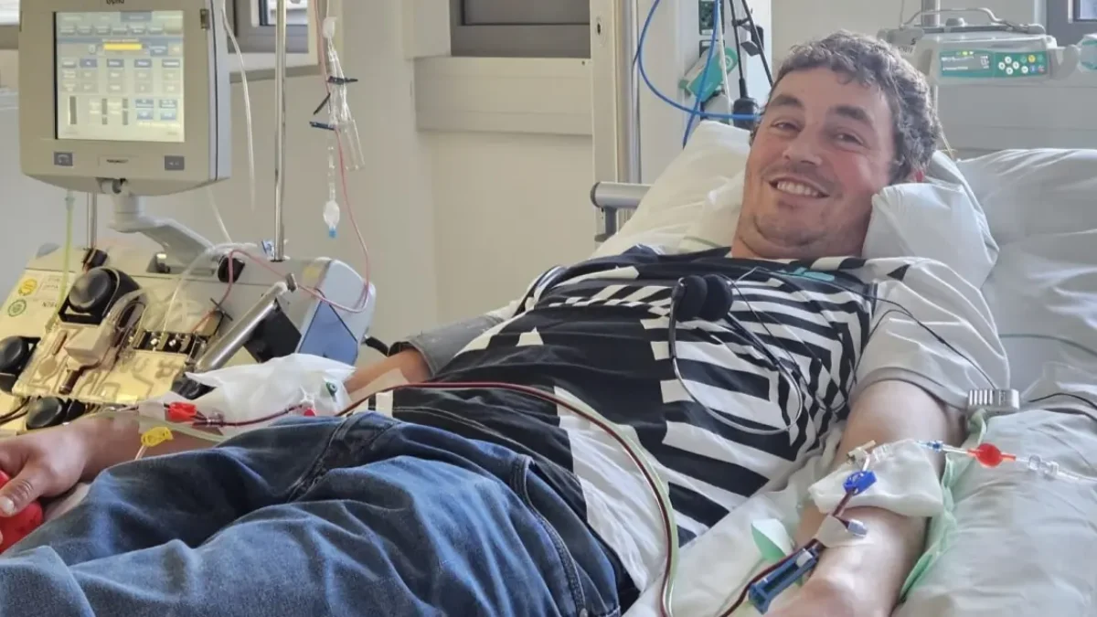 Ein Bild auf 5min.at zeigt, wie Manfred in einem Krankenbett liegt und lacht. In seiner Hand steckt eine Infusionsnadel.