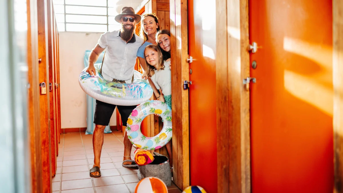 Ein Bild auf 5min.at zeigt vier Personen, darunter zwei Erwachsene und zwei Kinder, welche in Badeklamotten aus einer Strandbad-Kabine schauen. Um sie herum liegen Wasserbälle und und -ringe.
