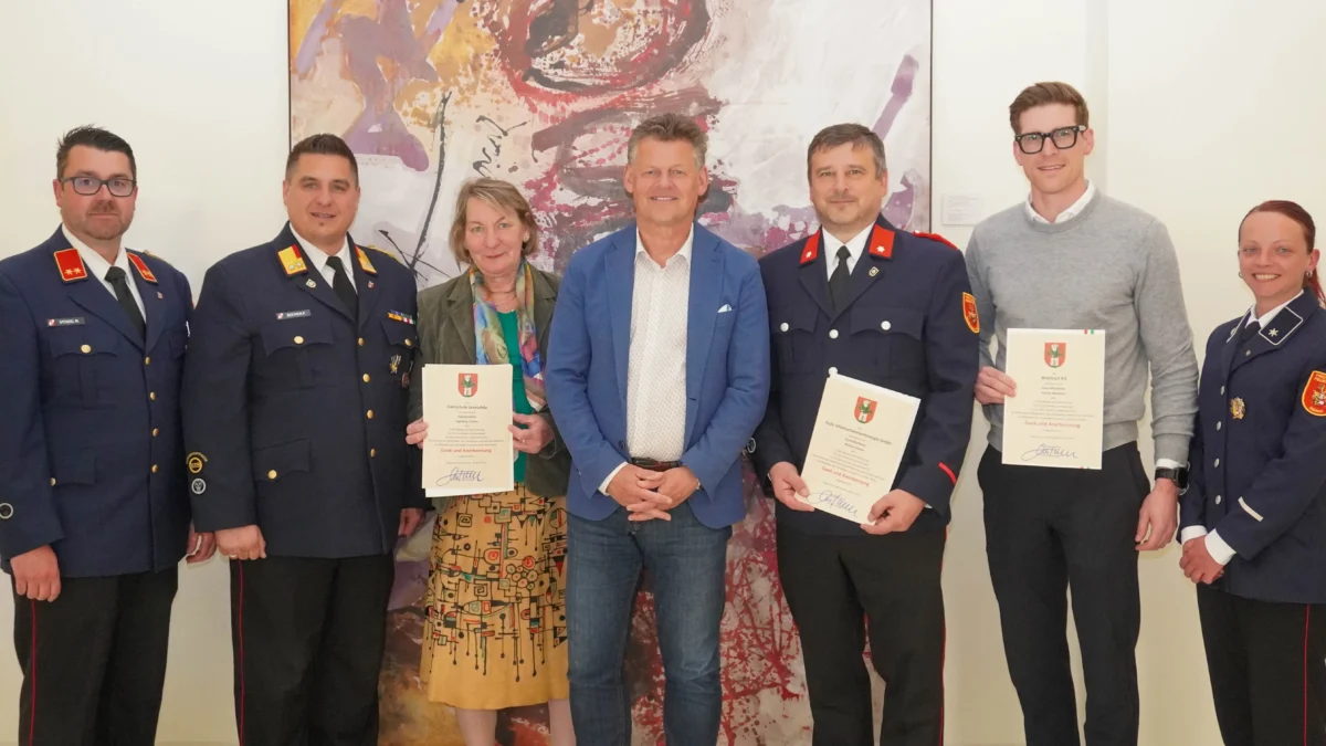 Ein Bild auf 5min.at zeigt vier Männer in Feuerwehrkleidung, eine Frau und einen Mann in Alltagskleidung und Bürgermeister Christian Scheider. Sie halten Urkunden in den Händen.