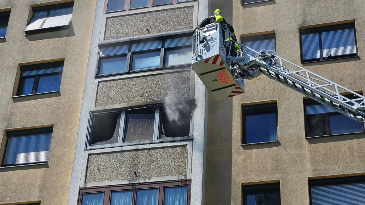 Ein Bild auf 5min.at zeigt, wie Rauch aus der Wohnung eines Mehrparteienhauses aufsteigt. Die Drehleiter ist davor positioniert.